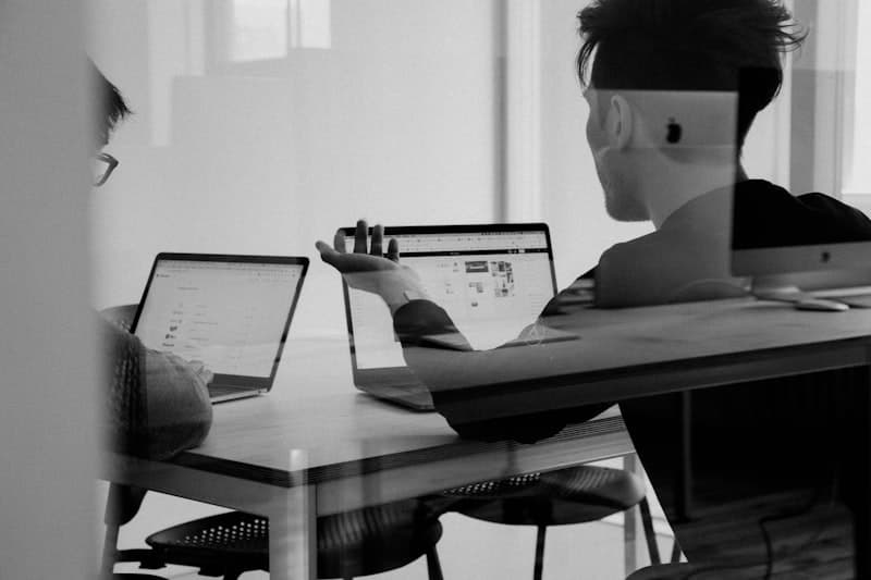 Two people collaborating at a desk with laptops